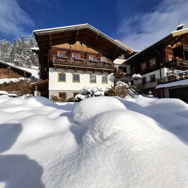 Der Bauernhof im Winter, mit traditioneller Holzarchitektur, Balkonen und einer verschneiten Umgebung.
