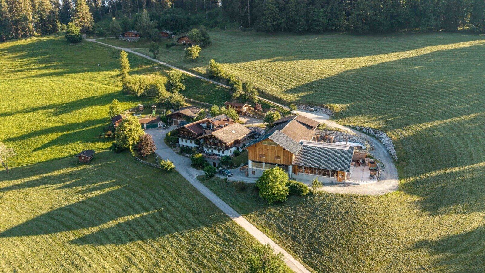 Ein idyllischer Bauernhof, umgeben von weitläufigen, saftig grünen Wiesen im warmen Sonnenlicht.