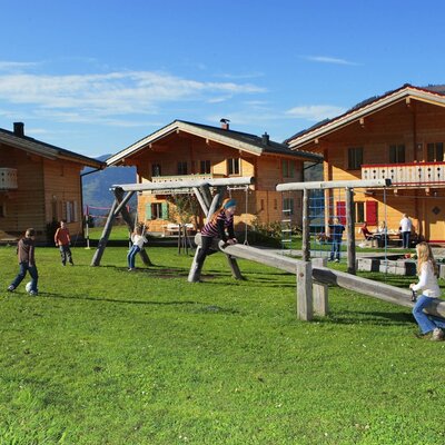 Der Bauernhof bietet einen Spielplatz mit Schaukeln, Wippe und Rasenfläche vor den Holzhäusern.