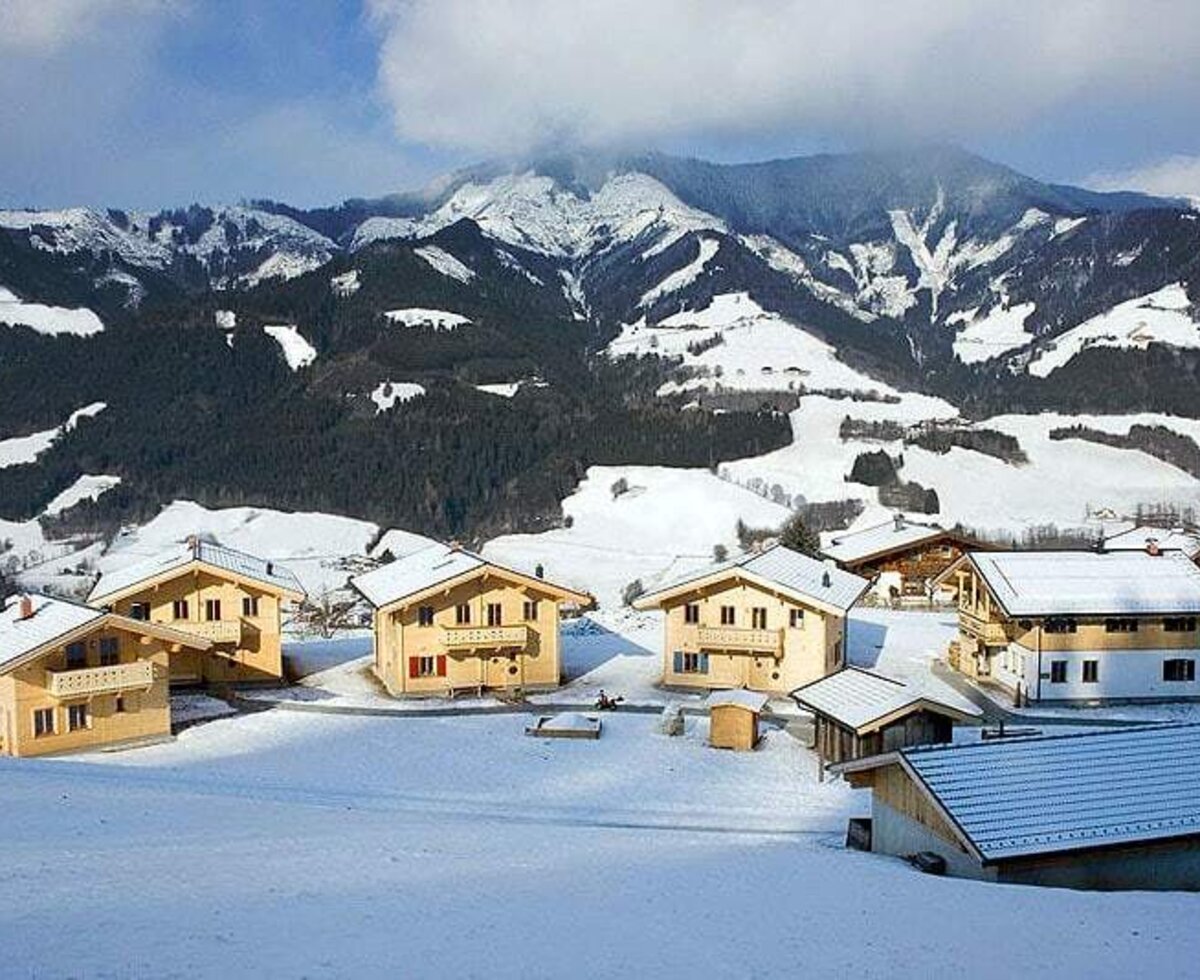 Die Holzhäuser des Ferienhofs in der verschneiten Winterlandschaft mit Bergblick.