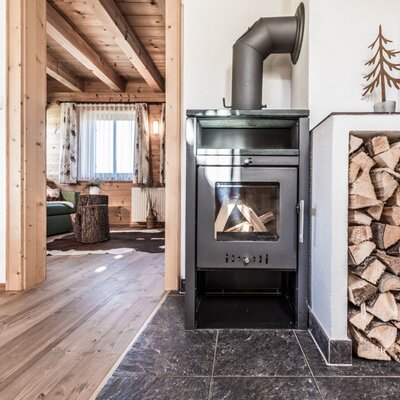 Holzofen mit Brennholz im Bauernhof, der in einen Wohnbereich mit Holzelementen führt.