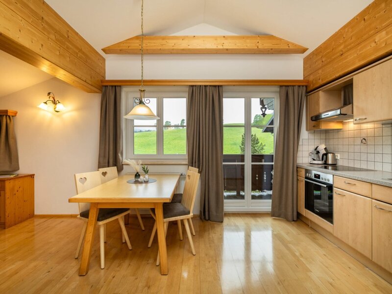 Voll ausgestattete Küche und Essbereich im Appartement mit Holztisch, modernen Geräten und Zugang zu einem Balkon mit Naturblick.