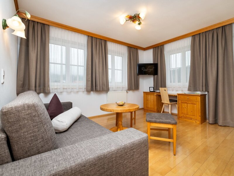 Wohnbereich eines Appartements auf dem Bauernhof mit Sofa, Couchtisch, Schreibtisch, Fernseher und Holzboden.