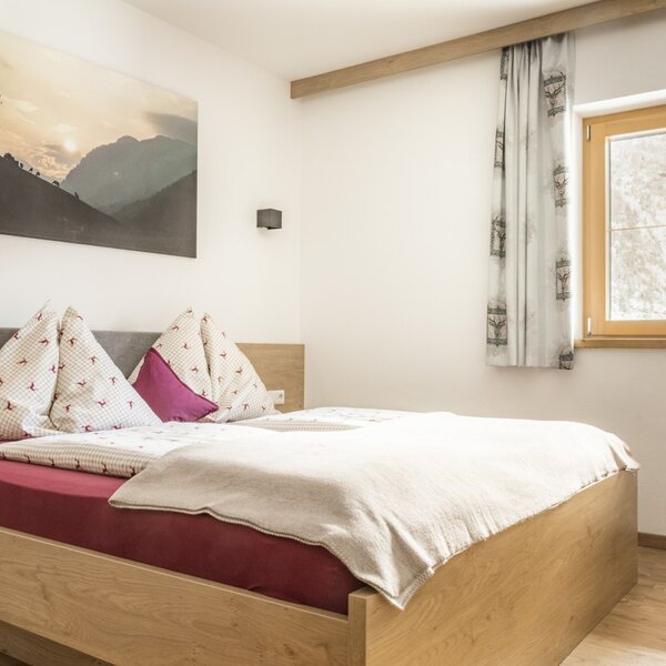 Schlafzimmer mit Doppelbett, Nachttisch und Fenster mit Vorhängen.