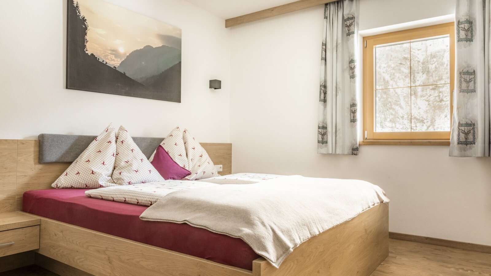 Schlafzimmer mit Doppelbett, Nachttisch und Fenster mit Vorhängen.
