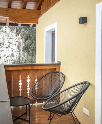 Balkon des Bauernhofs mit zwei Stühlen, einem Tisch und Blick auf verschneite Bäume.