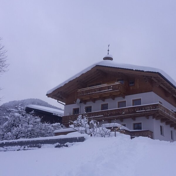 Der Bauernhof mit schneebedecktem Dach und Balkonen inmitten einer tief verschneiten Landschaft.