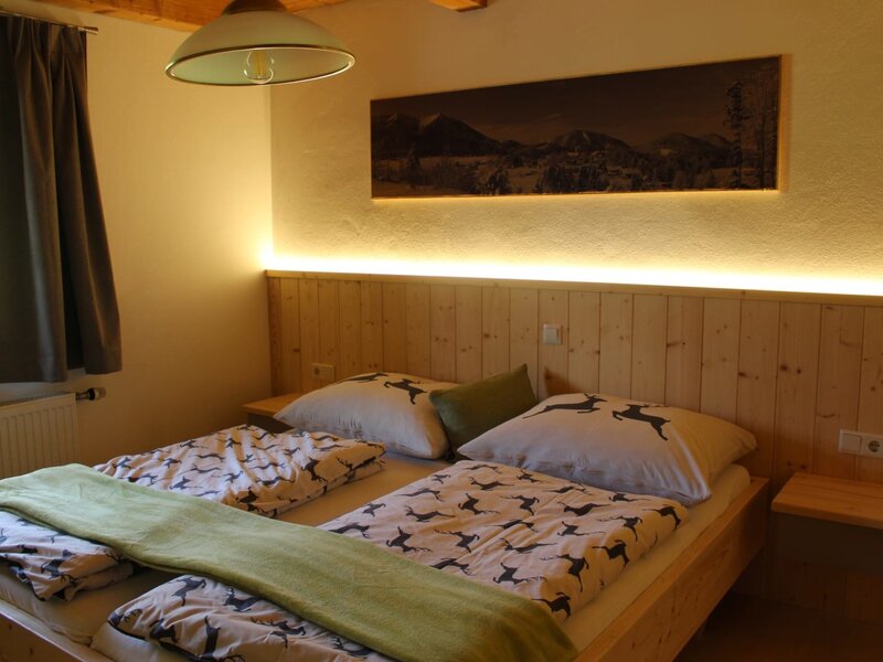 Ein gemütliches Doppelzimmer im Bauernhof mit einem warm beleuchteten Holzkopfteil und rustikal gemusterter Bettwäsche.