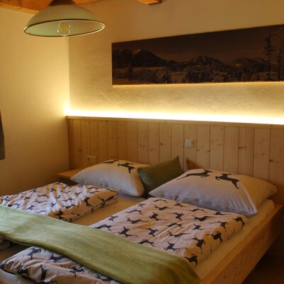 Ein gemütliches Doppelzimmer im Bauernhof mit einem warm beleuchteten Holzkopfteil und rustikal gemusterter Bettwäsche.