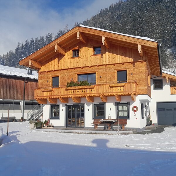 Der Bauernhof mit Holzfassade, Balkonen, einer Terrasse mit Sitzgelegenheiten und einer Garage im Winter.