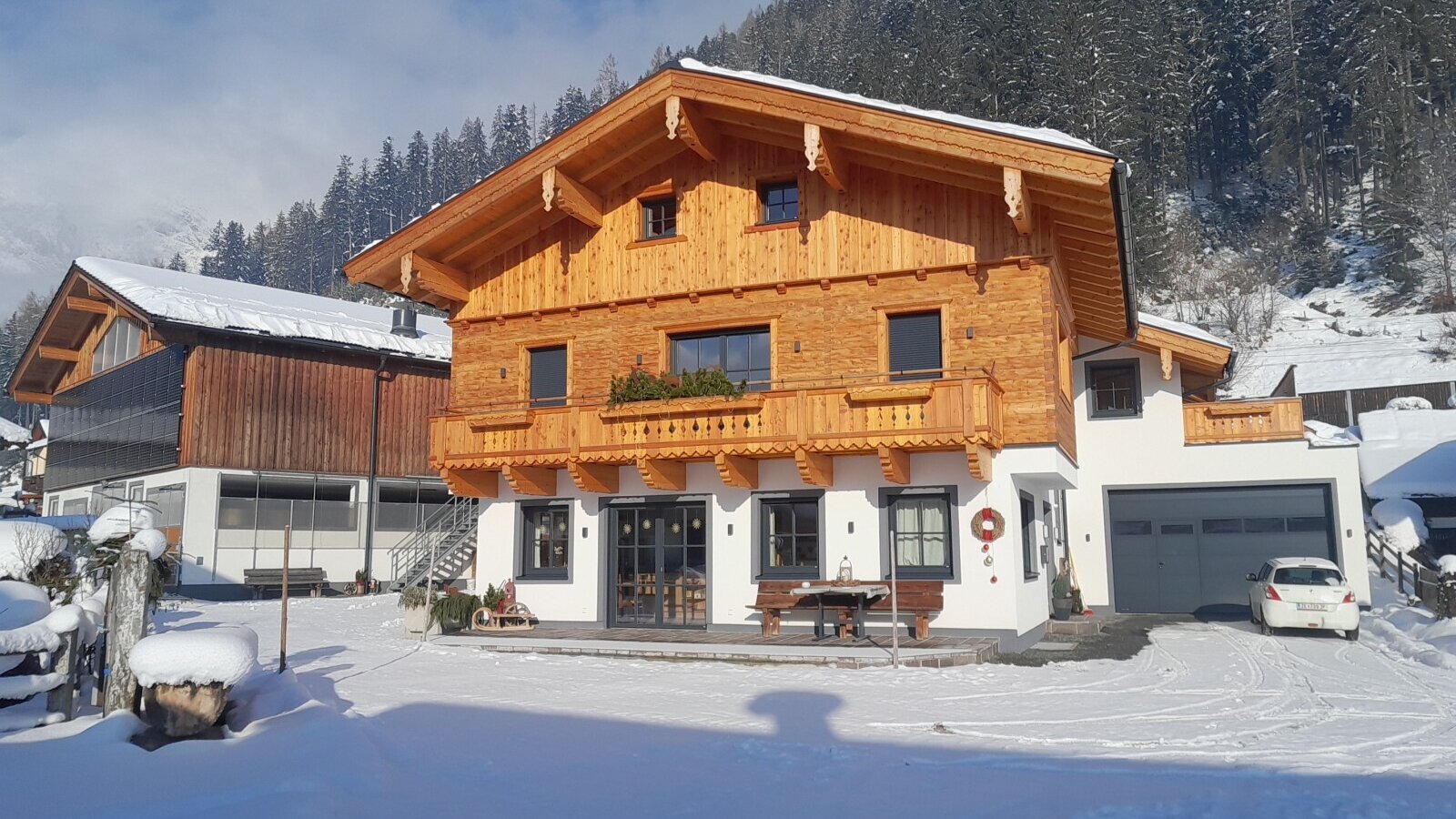 Der Bauernhof mit Holzfassade, Balkonen, einer Terrasse mit Sitzgelegenheiten und einer Garage im Winter.