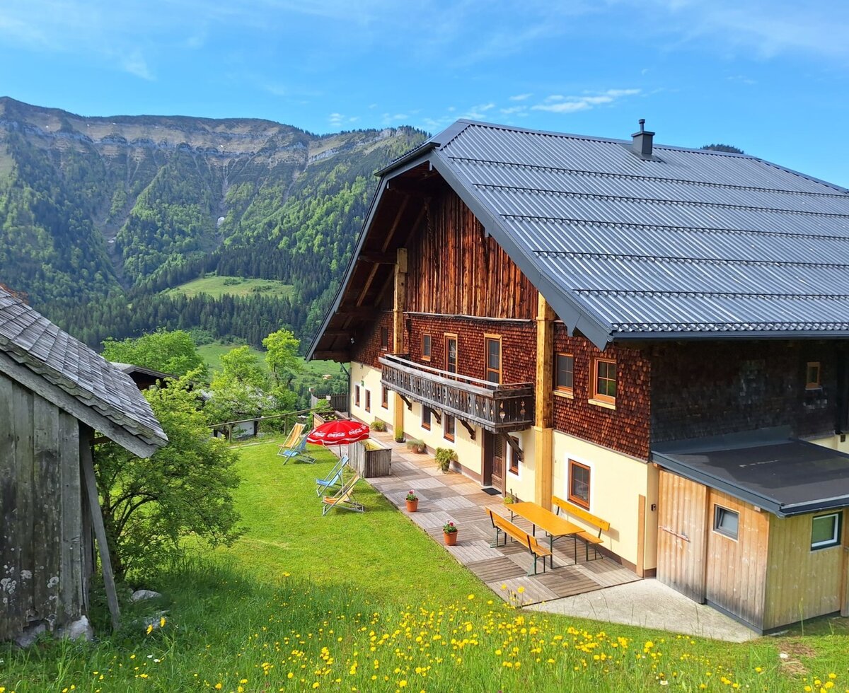 Der Bauernhof von außen mit Terrasse, Picknicktisch, Liegewiese und Bergblick.