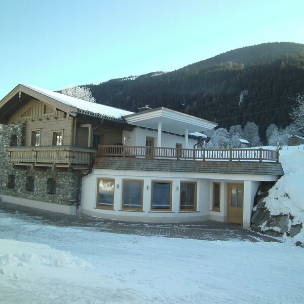 Der Bauernhof im Winter mit Holzbalkon, großer Terrasse und Blick auf die verschneite Berglandschaft.
