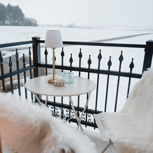 Balkon des Bed and Breakfast mit einem Tisch, zwei Stühlen mit Kunstfell und Blick auf eine verschneite Landschaft.
