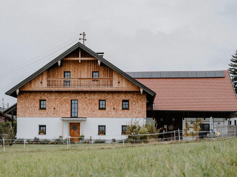Die traditionelle Holzfassade des restaurierten Bauernhofs mit Balkon und angrenzendem Gebäudeteil.