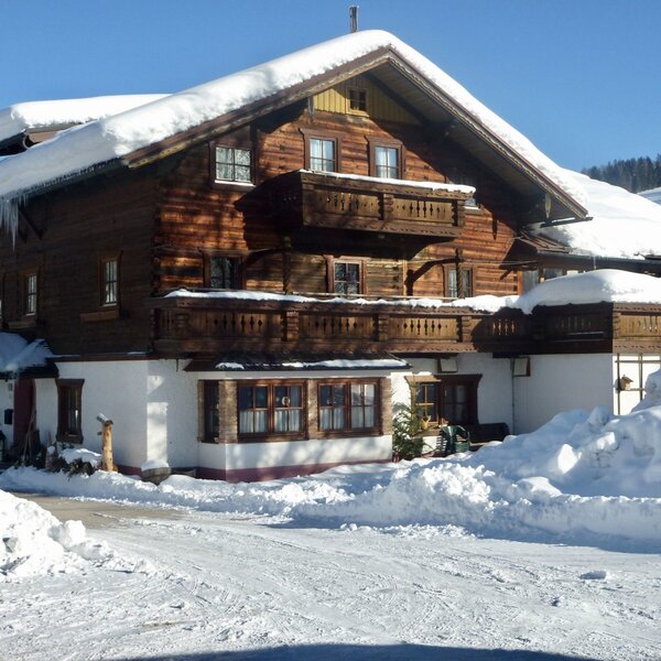 Aussenansicht des Bauernhofs mit traditioneller Holzfassade und Balkonen, bedeckt mit Schnee im Winter.