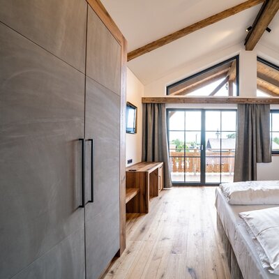 Geräumiges Doppelzimmer im Bauernhof mit Doppelbett, Kleiderschrank, SAT-TV, hohen Decken mit Holzbalken und Zugang zu einem Balkon.