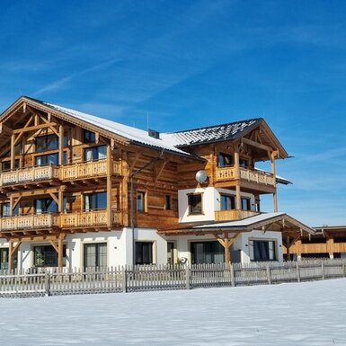 Der Bauernhof mit seiner Holzfassade, mehreren Balkonen und verschneiten Dächern im Winter.