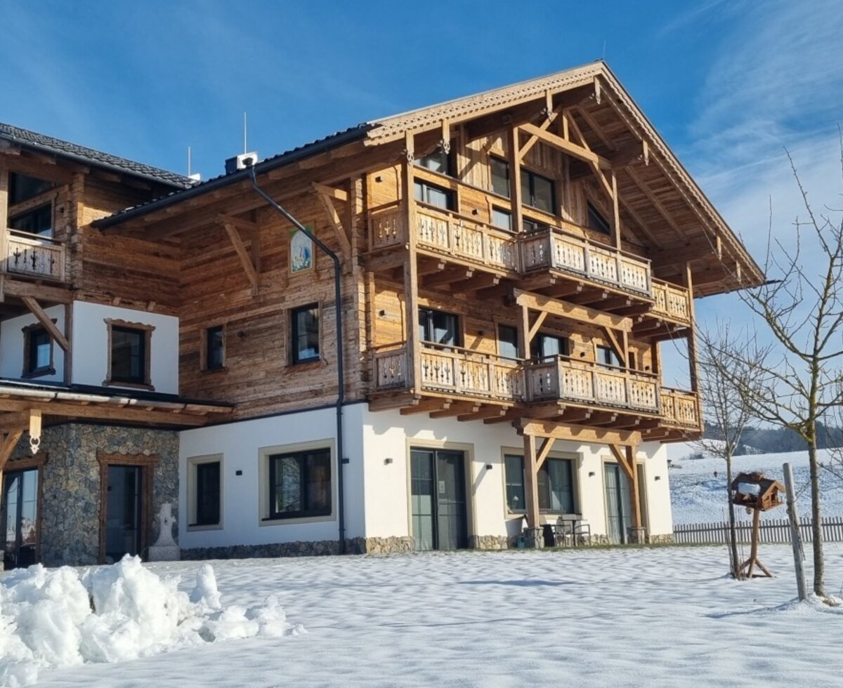 Der Bauernhof in winterlicher Landschaft mit mehreren Balkonen.