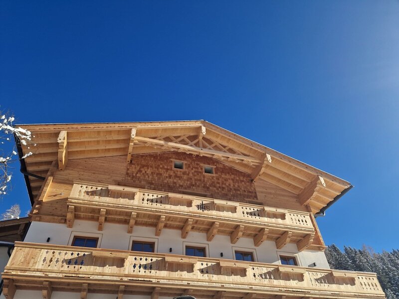 Die Fassade des Bauernhofs mit mehreren Holzbalkonen und traditioneller Holzverkleidung.