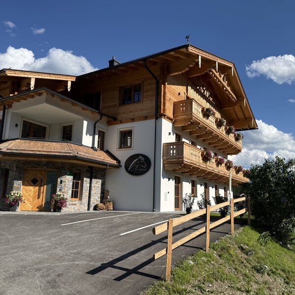 Der einladende Bauernhof mit seiner traditionellen Holzfassade und blumengeschmückten Balkonen vor einem strahlend blauen Himmel.