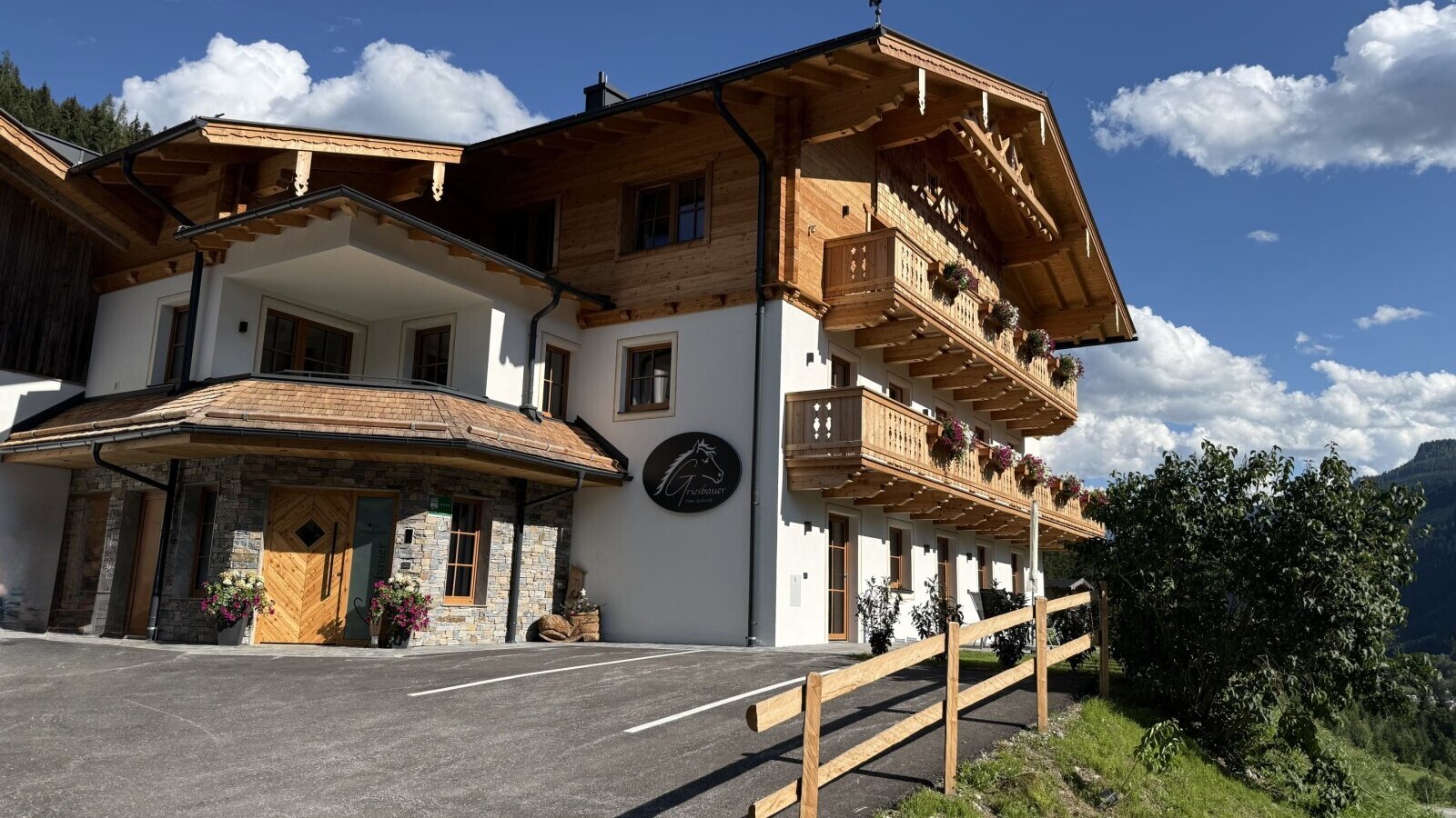 Der einladende Bauernhof mit seiner traditionellen Holzfassade und blumengeschmückten Balkonen vor einem strahlend blauen Himmel.