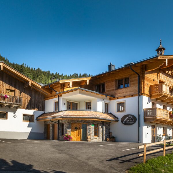 Der einladende Bauernhof mit traditionellen Holzbalkonen vor einer malerischen Bergkulisse.