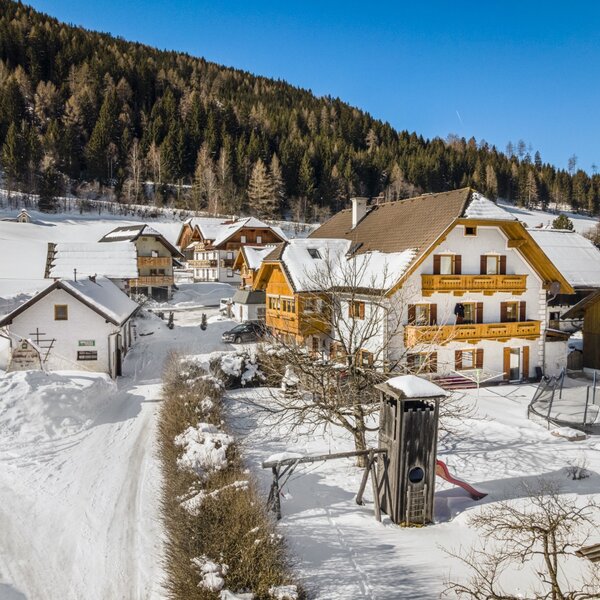 Der Bauernhof mit umliegenden Gebäuden, Balkonen und einem schneebedeckten Garten mit Spielturm und Trampolin.
