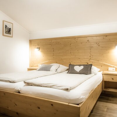 Helles Schlafzimmer mit Doppelbett, Holzrahmen, Holzkopfteil, Nachttischen, Leselampen und einem Bild an der Wand.