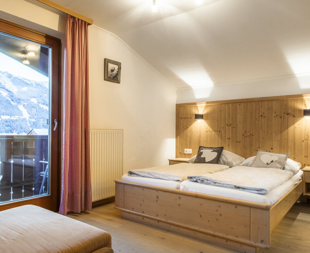 Doppelbettzimmer mit Holzeinrichtung, Balkonzugang und Bergblick.