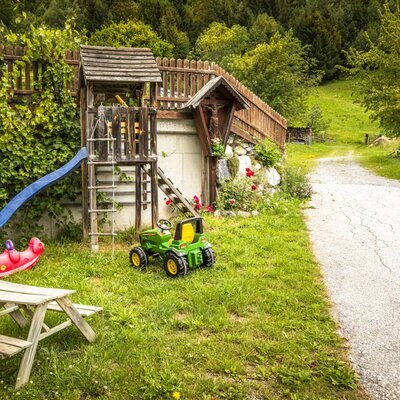 Der einladende Spielbereich des Bauernhofs mit einer Rutsche, Schaukel und einem kleinen Picknicktisch im Grünen.