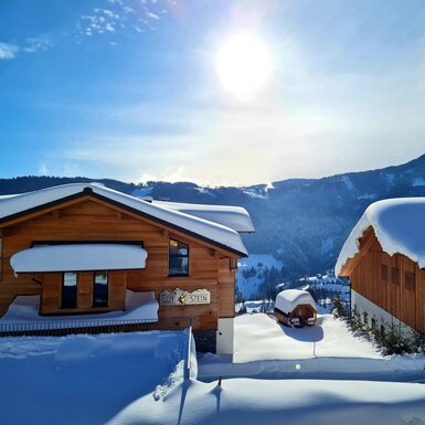 Außenansicht des Bauernhofs im Winter mit schneebedeckten Dächern und umliegenden Bergen.