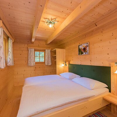 Schlafzimmer im Bed and Breakfast mit Doppelbett, Holzwänden, Holzbalkendecke und Fenstern mit Vorhängen.