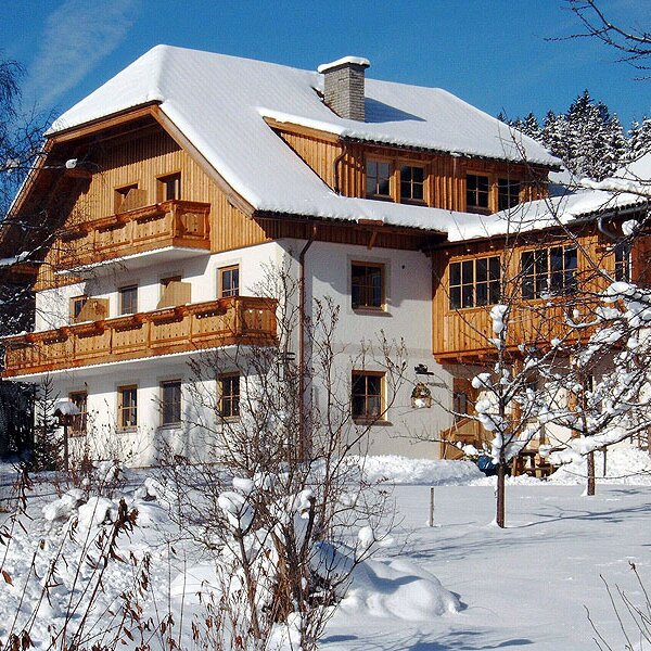 Die Außenansicht des Bauernhofs im Winter mit verschneiten Bäumen und Balkonen.