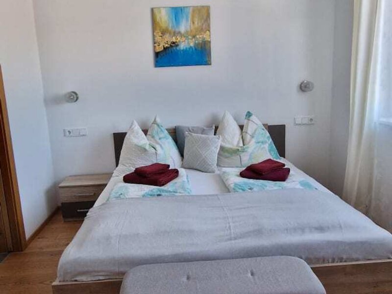 Schlafzimmer mit Doppelbett, zwei Nachttischen, Wandlampen und einer Sitzbank.