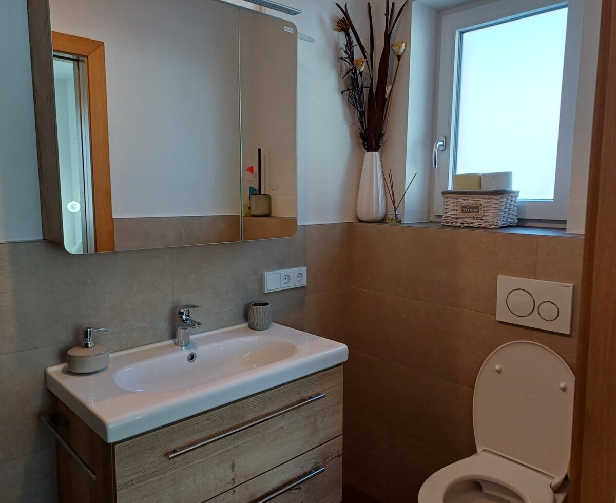 Badezimmer mit Waschbecken, Unterschrank, Spiegelschrank, Toilette und Fenster.