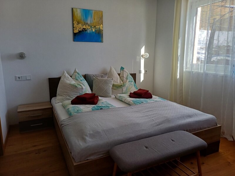 Doppelbett mit Nachttischen, einer Sitzbank und einem Fenster mit Vorhängen in diesem Bed and Breakfast.