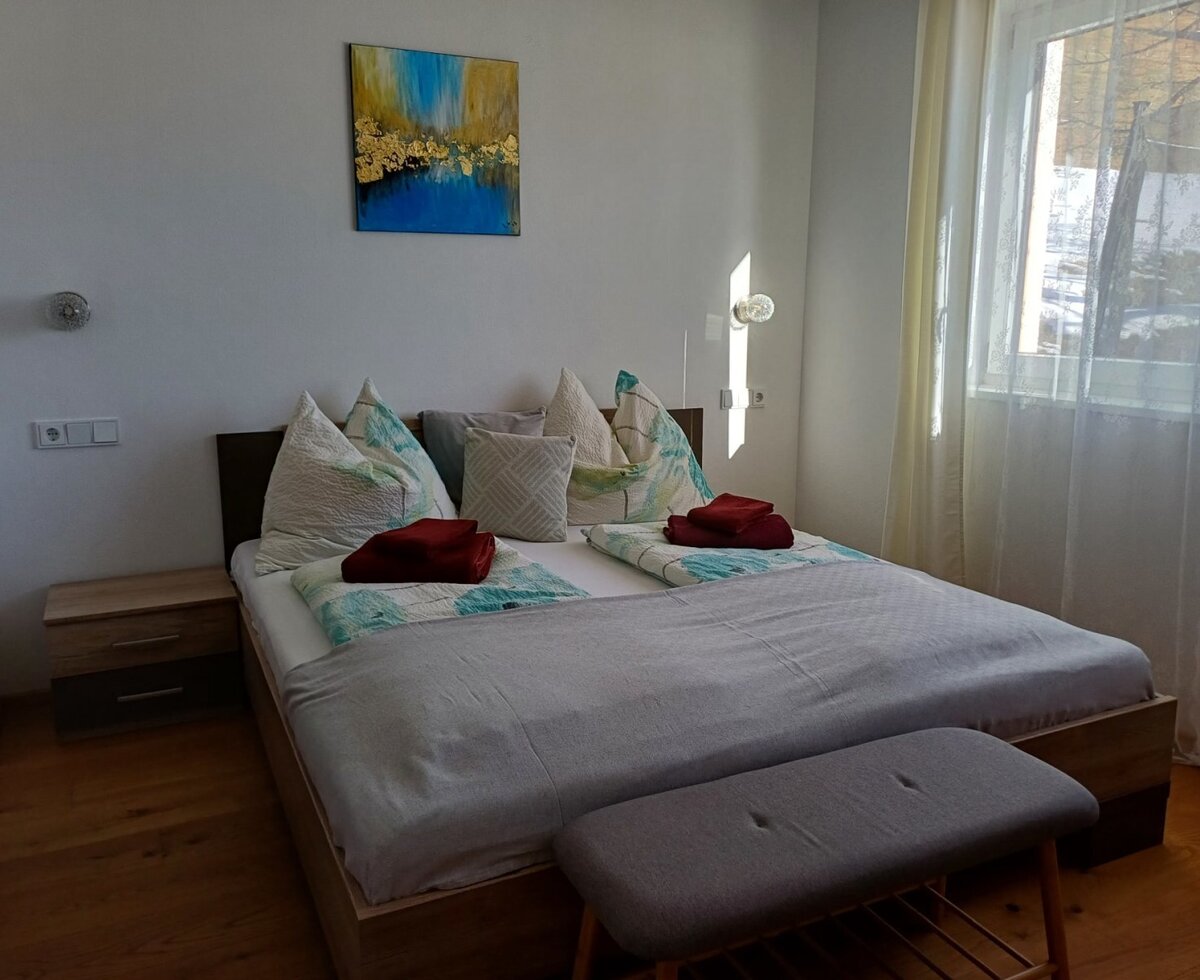 Doppelbett mit Nachttischen, einer Sitzbank und einem Fenster mit Vorhängen in diesem Bed and Breakfast.