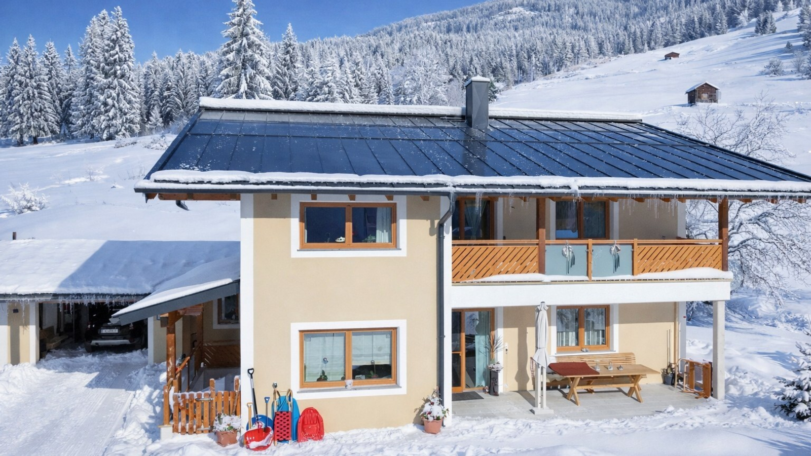 Außenansicht  im Winter mit schneebedeckter Landschaft, einem Balkon im Obergeschoss und einer Terrasse im Erdgeschoss.