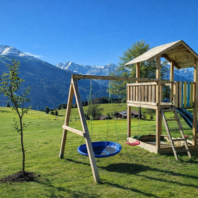 Kinderspielplatz mit Schaukel, Rutsche und Spielturm vor einer Bergkulisse.