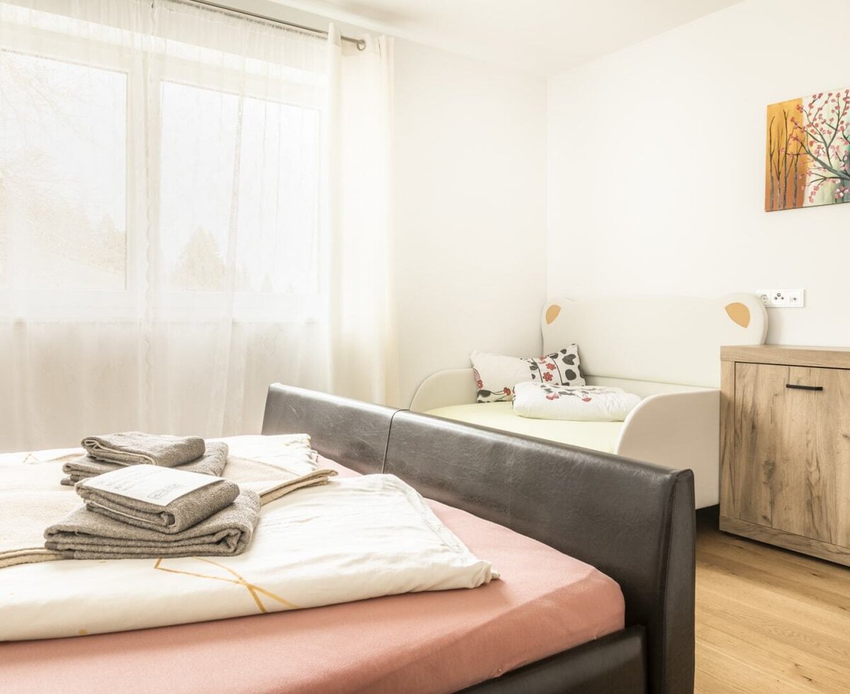 Schlafzimmer im Bed and Breakfast mit Doppelbett, Einzelbett, Holzkommode und Fenster mit transparenten Vorhängen.