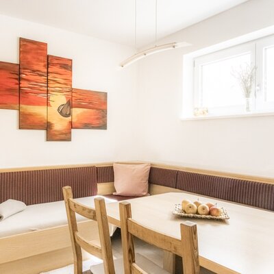 Essbereich in der Gemeinschaftsküche mit gepolsterter Eckbank, Holztisch und Stühlen neben einem Fenster.