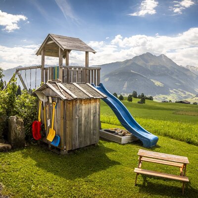 Der einladende Kinderspielplatz des Bed and Breakfasts mit Rutsche und Schaukel vor einer malerischen Bergkulisse.