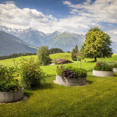 Der gepflegte Garten des Bed and Breakfasts mit runden Hochbeeten und malerischem Blick auf die umliegenden Berge.