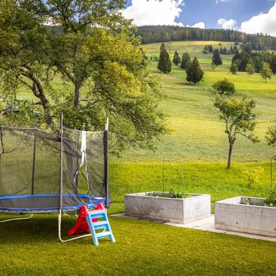 Der einladende Garten des Bed and Breakfasts mit einem Trampolin, Hochbeeten und Blick auf die sanften, grünen Hügel.