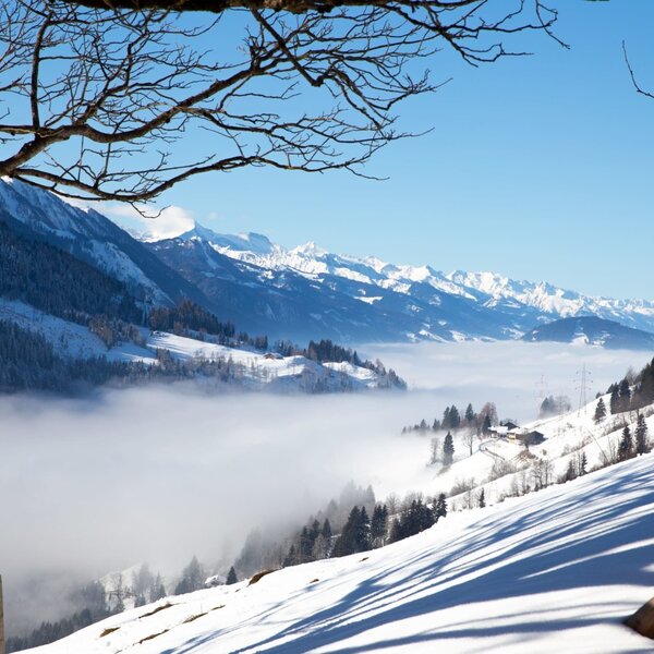 Blick auf die winterliche Berglandschaft mit Talnebel und schneebedeckten Gipfeln.