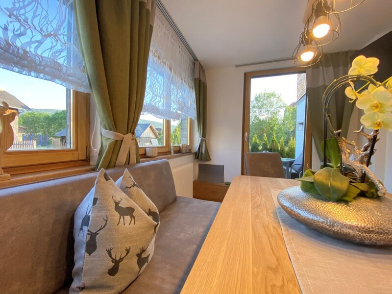 Essbereich im Bauernhof mit Holztisch, Sitzbank, Fensterblick auf die Umgebung und Zugang zu einem Außenbereich.