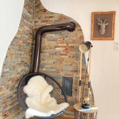 Im Bauernhof finden Sie einen Kaminofen mit Steinwand, einen Sessel mit Schaffell und eine Wanddekoration mit Hirschkopf.