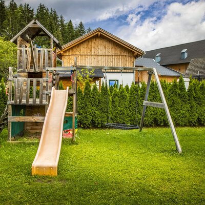 Der Spielplatz des Bauernhofs mit Rutsche und Schaukel auf einer Rasenfläche.