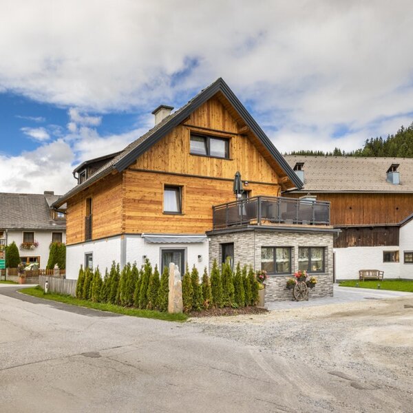 Außenansicht des Bauernhofs mit Holzfassade, Balkon und Schotterparkplatz.